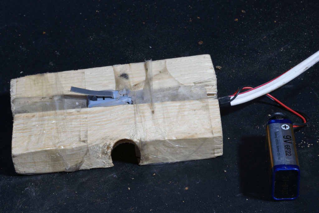 A switch made from a modified refrigerator door lightswitch attached to a plank of wood. This switch is usually placed under an attractive object or under the container full of explosives. When a person lifts the object, the pressure is released, which activates the detonator and causes the device to function.
