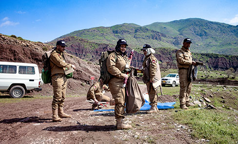 5 deminers in the field and the women in the center similing 5 deminers in the field and the women in the center similing