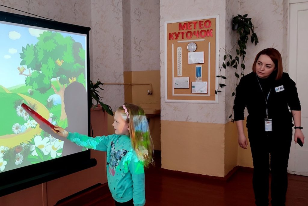 During an FSD risk education session, a little girl learns to spot explosive devices hidden in a landscape