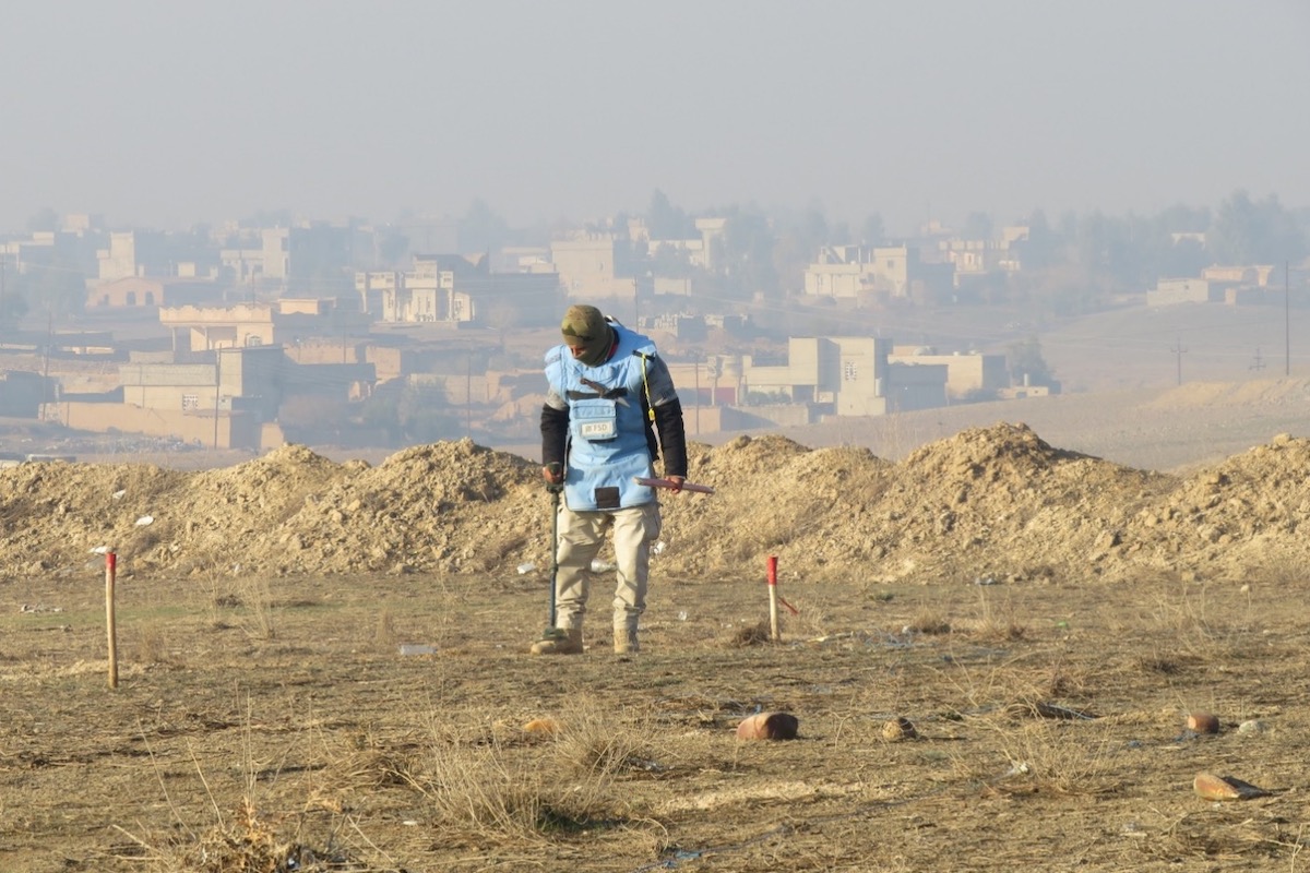 FSD Operator conducting metal detector clearance procedures with Khalidiya village in the background iraq