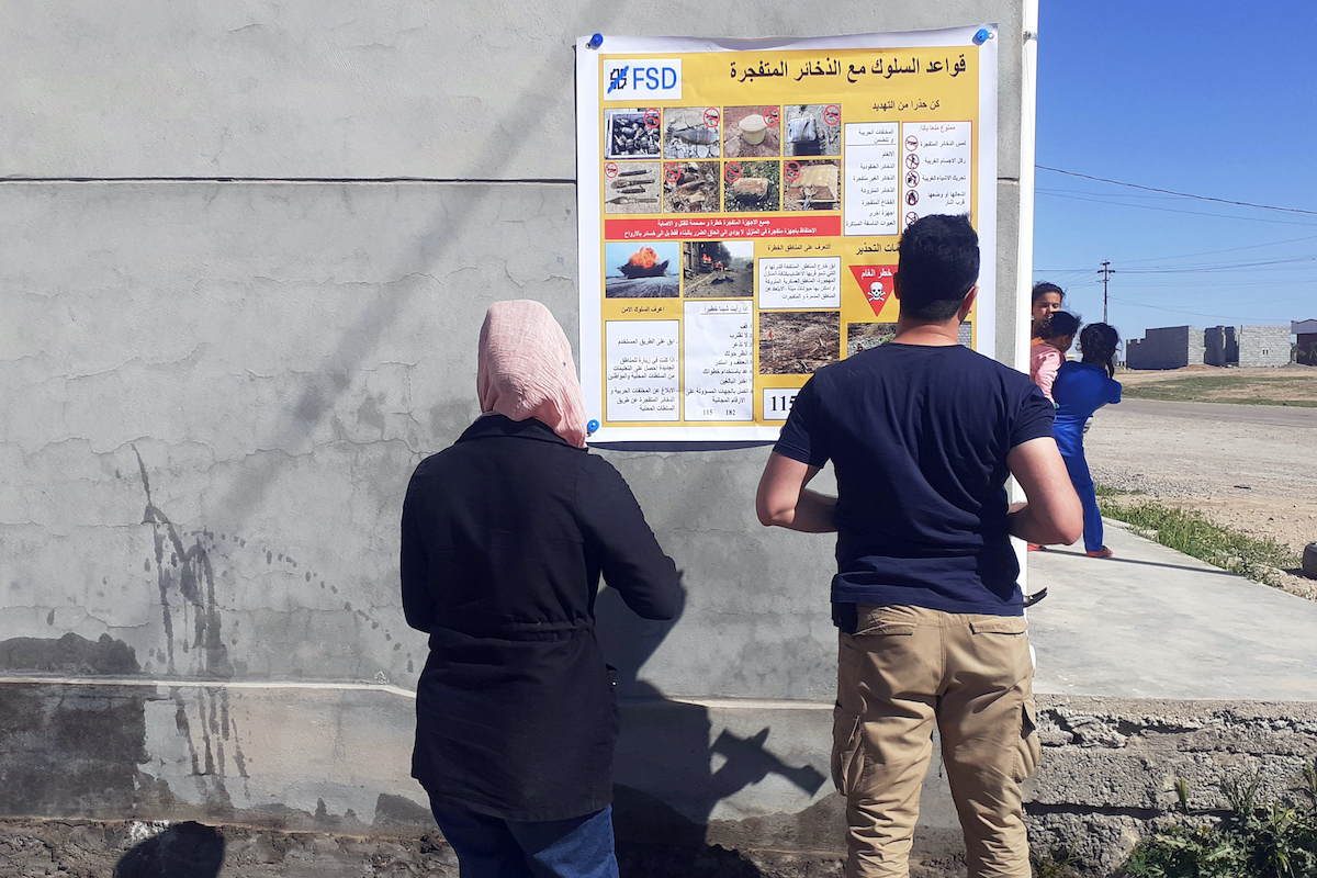 Villagers studying an EORE information poster in Iraq