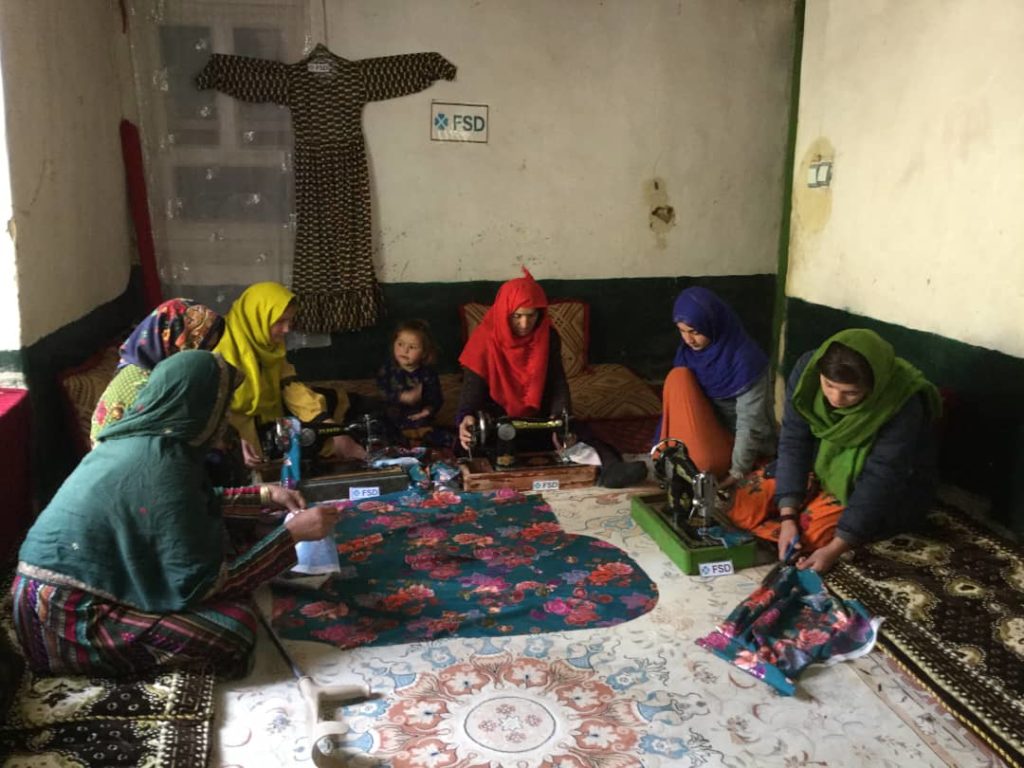 Women in saris sewing together at a table for Female Mine Victims Tailoring Training in Darwaz Bala, Badakhshan, NE Afghanistan