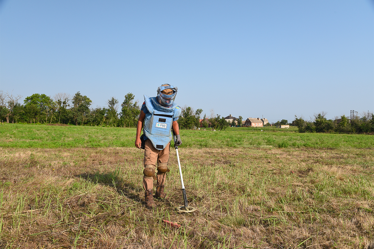 FSD Deminer searches in a field scanning for mines with a mine detector